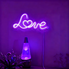 Neon sign with 'Love' on a purple wall with a lava lamp and plants below.