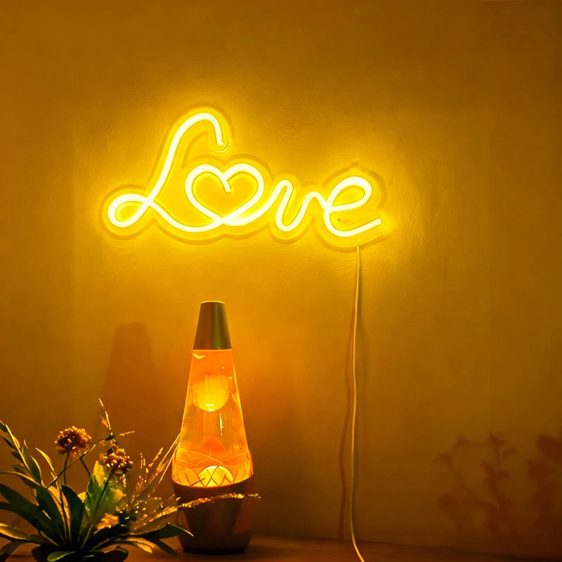 Neon sign spelling 'Love' with a lava lamp and plant on a yellow background