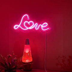 Neon sign with 'Love' on a pink wall next to a lava lamp