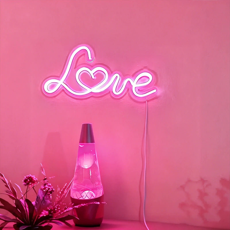 Neon sign spelling 'LOVE' on a light pink wall with a lava lamp and plant.
