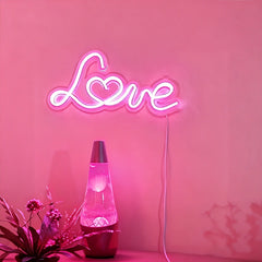 Neon sign spelling 'LOVE' on a light pink wall with a lava lamp and plant.