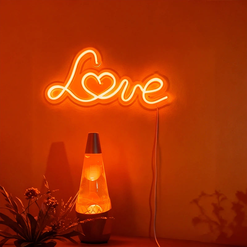 Neon sign spelling 'LOVE' on an orange wall with a lava lamp and plant in the foreground.