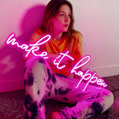 Person sitting on the floor with 'make it happen' neon sign in front