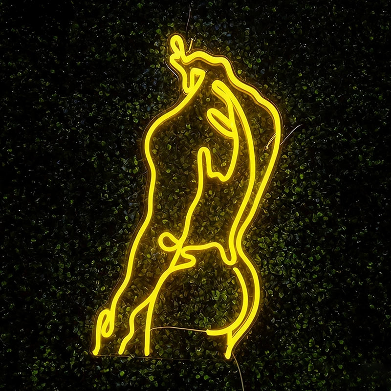 Lemon yellow neon line art sign of a stylized human figure against a dark leafy background, glowing brightly in the night.