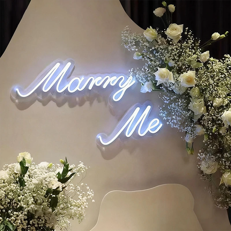 Neon 'Marry Me' sign with floral arrangements.