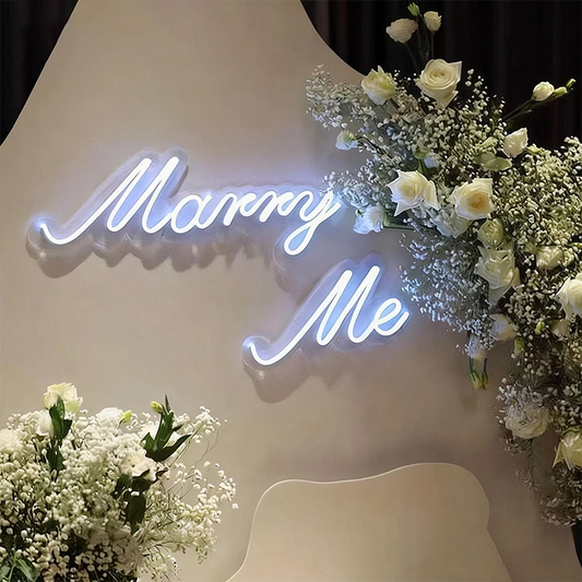 Neon 'Marry Me' sign with floral arrangements.