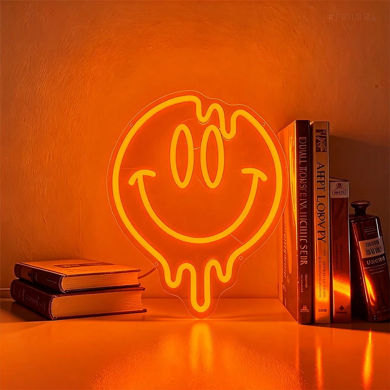 Neon light shaped like a smiley face on an orange background with books and a bottle.