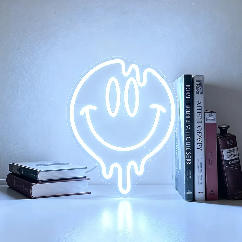 Neon light shaped like a smiley face with a drool effect, placed on a shelf among books and a bottle.