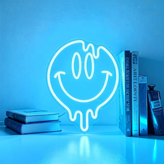 Neon light shaped like an ice blue smiley face on a shelf with books and a bottle.