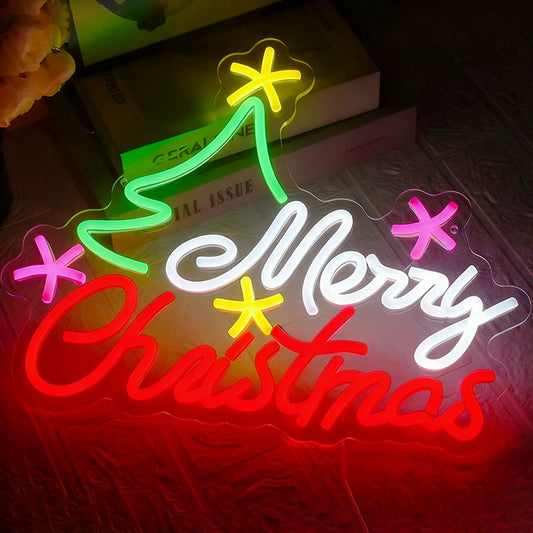 A glowing LED neon-style Christmas sign on a dark surface, with the words “Merry Christmas” in white and red script, a green tree shape, and pink and yellow star accents.