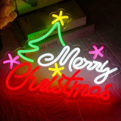 A glowing LED neon-style Christmas sign on a dark surface, with the words “Merry Christmas” in white and red script, a green tree shape, and pink and yellow star accents.