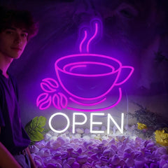 Neon sign of a coffee cup with steam and 'OPEN' text, glowing purple, on a decorative background.