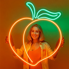 Woman holding a neon peach-shaped light against an orange and green gradient background