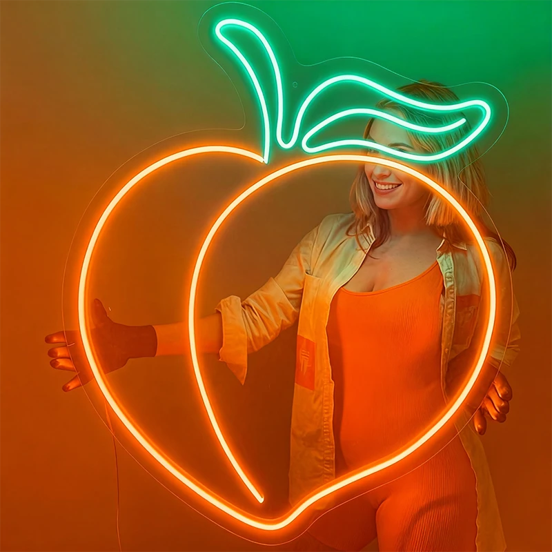 Woman holding a neon light shaped like a peach design against a gradient background.