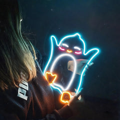 A person holding a glowing neon-style penguin-shaped light with a bright blue outline, white eyes, and orange accents against a dark background.