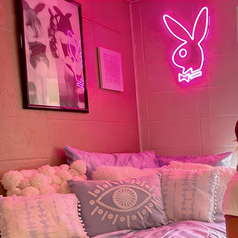 Neon Playboy sign in a room with pink walls and decorative pillows.