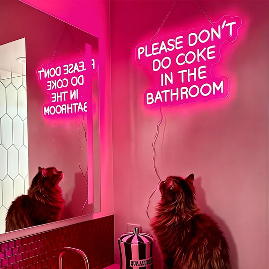 Neon sign in a bathroom with a cat looking at itself in the mirror.