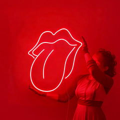 A person holding a glowing red rolling stone logo neon sign against a solid dark wall.