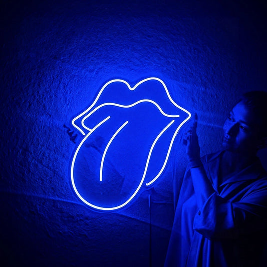 A blue neon sign shaped like the Rolling Stones tongue and lips, mounted on a textured wall, with a person in a white shirt standing to the right in a dimly lit room.