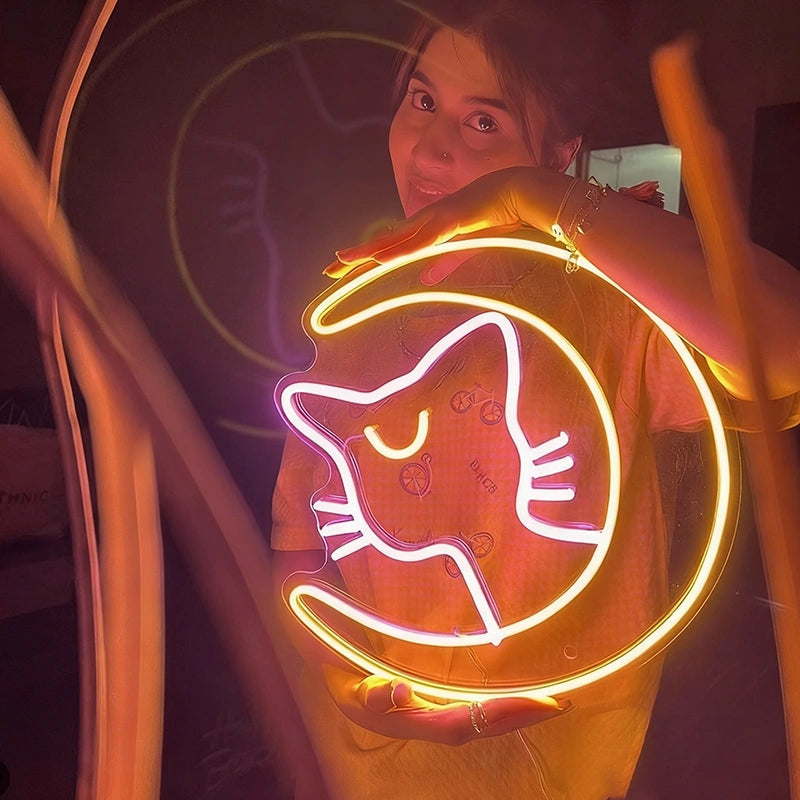 Person holding a neon sign shaped like a hot pink cat with lemon yellow luna moon in a dark setting