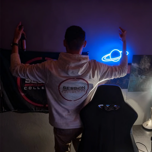 Person in a white hoodie with a visible brand logo, arms raised in a dark room with blue saturn neon light.