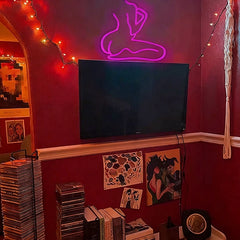 Neon sign of a sexy lady's silhouette on a red wall with a TV and records below.