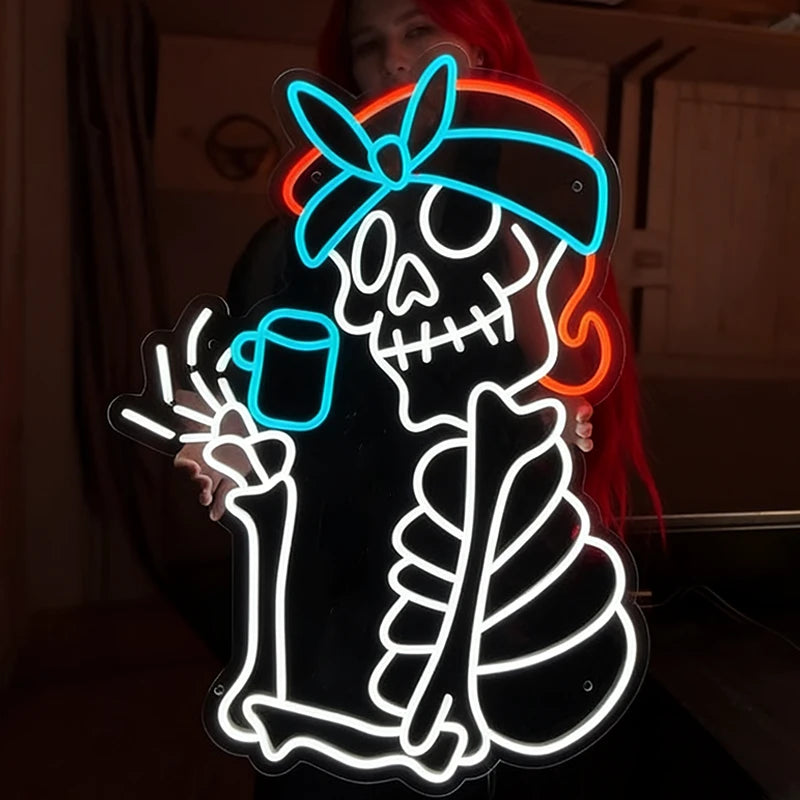 A large neon-style sign featuring a cartoon skeleton pirate with a blue bandana, white bones, and orange hair, shown in a dim indoor setting with a person holding it behind the illuminated figure.