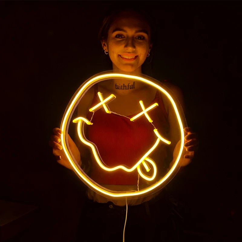Person holding a lemon yellow smiley face neon sign on a dark background