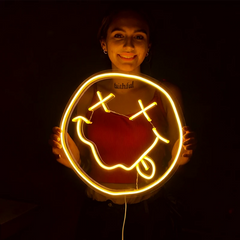 Person holding a lemon yellow smiley face neon sign on a dark background