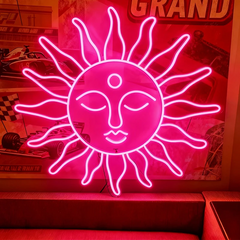 Neon hot pink sun-shaped sign with face design on a red background