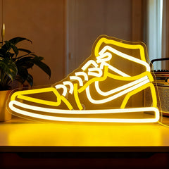 Neon light shaped like a high-top sneaker on a wooden surface with a plant and radio in the background.
