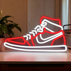 Neon sign of a sneaker on a table with a plant and radio in the background