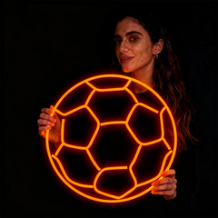 Woman holding a neon orange soccer ball against a black background