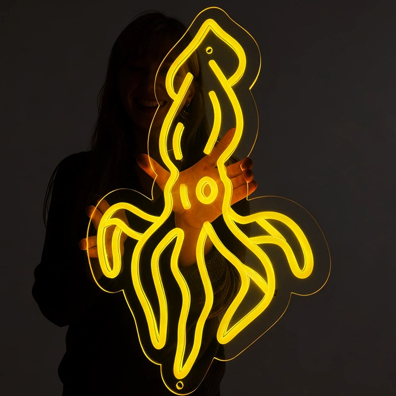 Person holding a lemon yellow squid neon sign in a dark background.