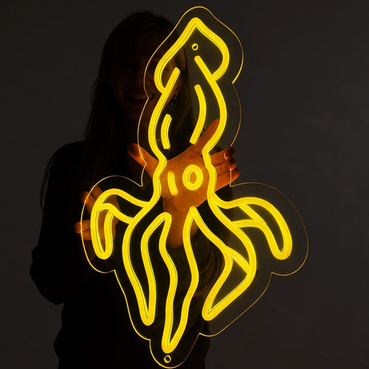 Person holding a lemon yellow squid neon sign in a dark background.