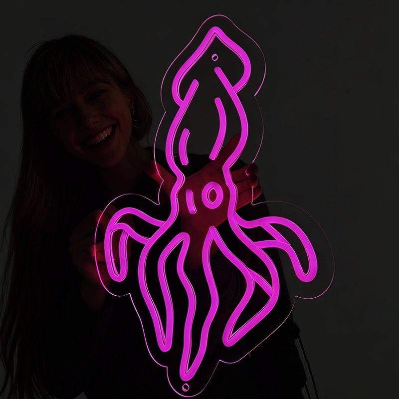 Person holding a hot pink color squid neon sign in a dark background.