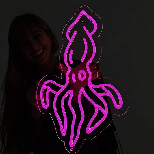 Person holding a hot pink color squid neon sign in a dark background.