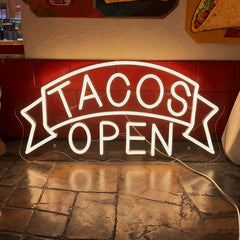 Glowing neon sign with 'TACOS OPEN' text in a mexican restaurant