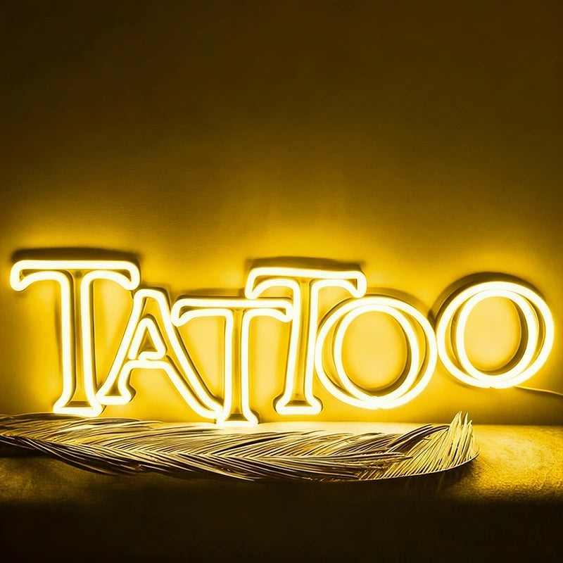 Neon sign spelling 'Tattoo' with feathers on a yellow background