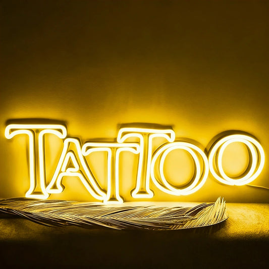 Neon sign spelling 'Tattoo' with feathers on a yellow background