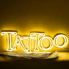 Neon sign spelling 'Tattoo' with feathers on a yellow background