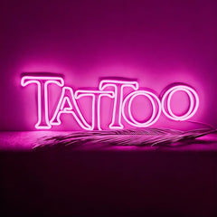 Neon sign spelling 'Tattoo' on a pink background with a feather.