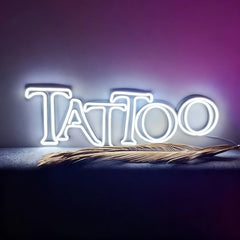 Neon sign spelling 'Tattoo' with a feather on a dark background