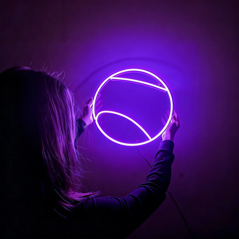 Person holding a round purple tennis ball neon light against a dark background
