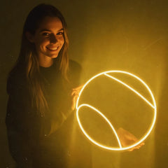 Woman holding a glowing lemon yellow neon tennis ball against a drak background