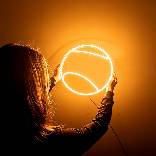 Person holding a round warm white tennis ball neon light against a dark background