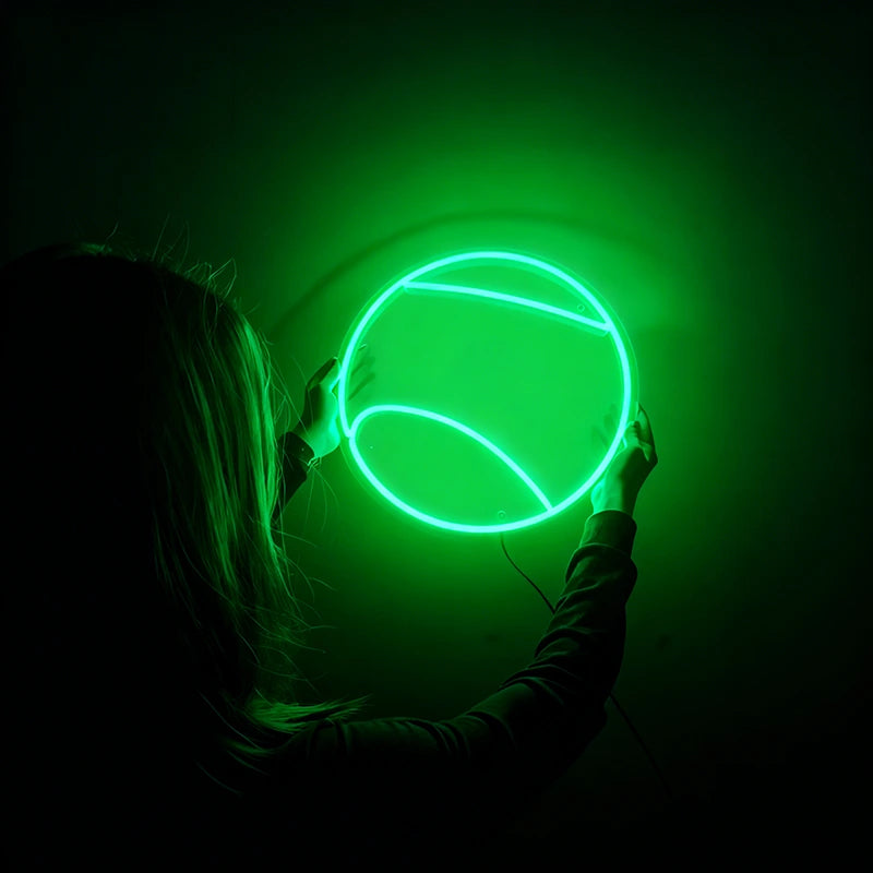Person holding a round green tennis ball neon light against a dark background