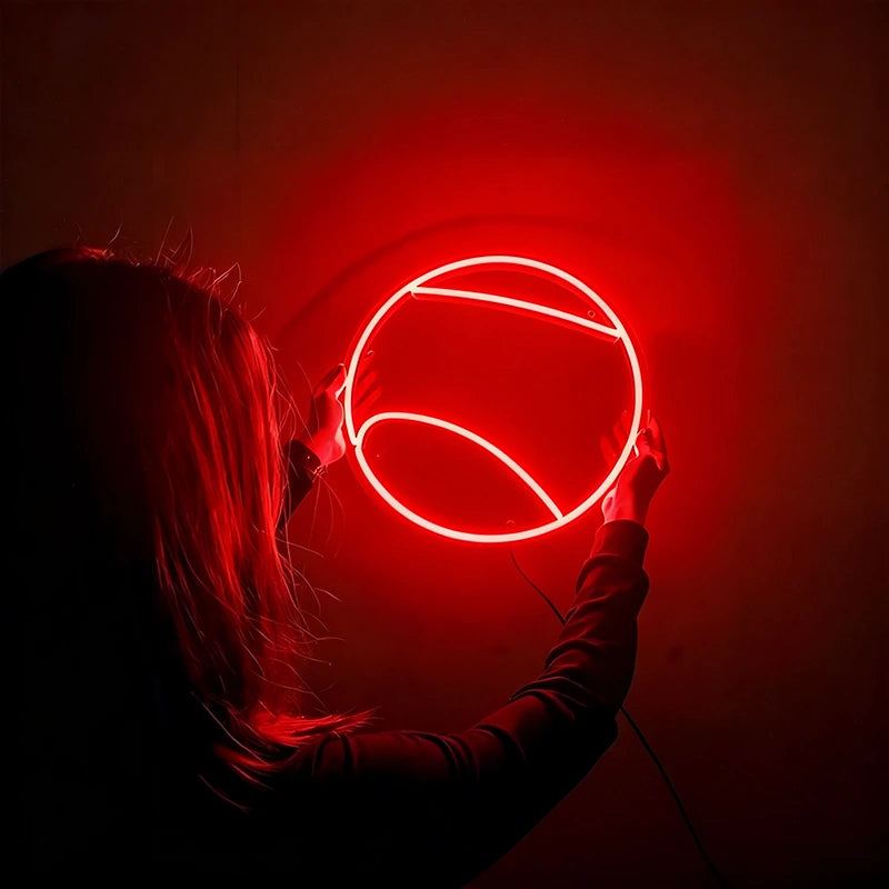 Person holding a round red tennis ball neon light against a dark background