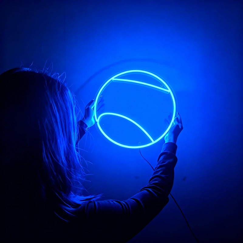Person holding a round blue tennis ball neon light against a dark background