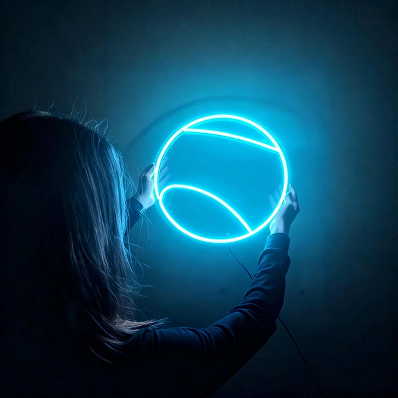 Person holding a round ice blue tennis ball neon light against a dark background